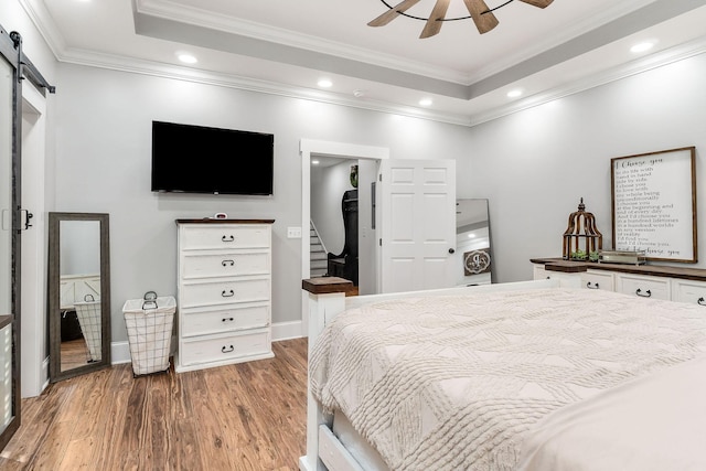 bedroom featuring wood-type flooring, ornamental molding, a raised ceiling, a spacious closet, and a barn door