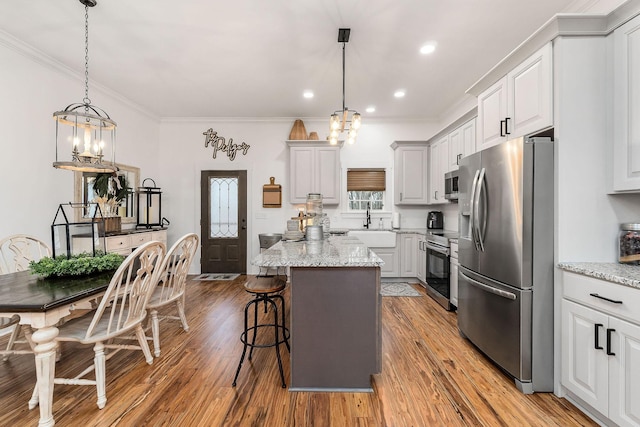 kitchen with a breakfast bar, hanging light fixtures, stainless steel appliances, a center island, and light stone countertops