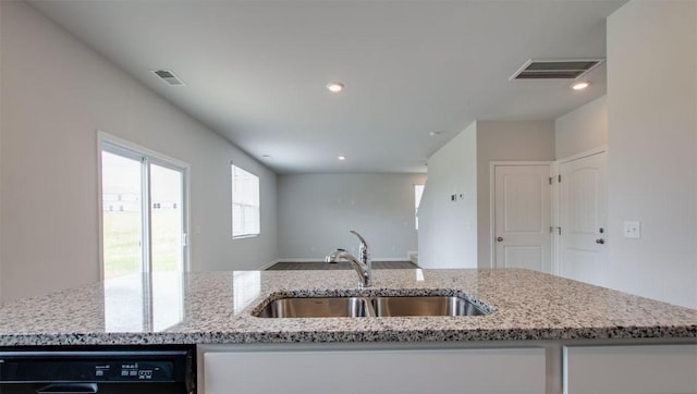 kitchen featuring a kitchen island with sink, black dishwasher, sink, and light stone countertops