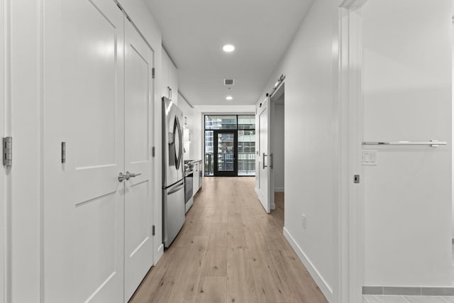 hallway with expansive windows, a barn door, and light hardwood / wood-style floors