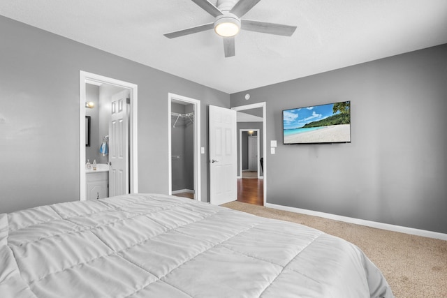 bedroom with ensuite bathroom, a spacious closet, ceiling fan, light carpet, and a closet