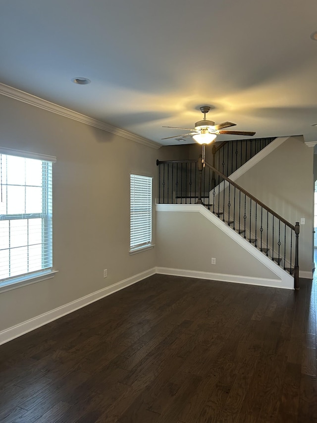 empty room featuring stairway, dark wood-type flooring, baseboards, and ornamental molding