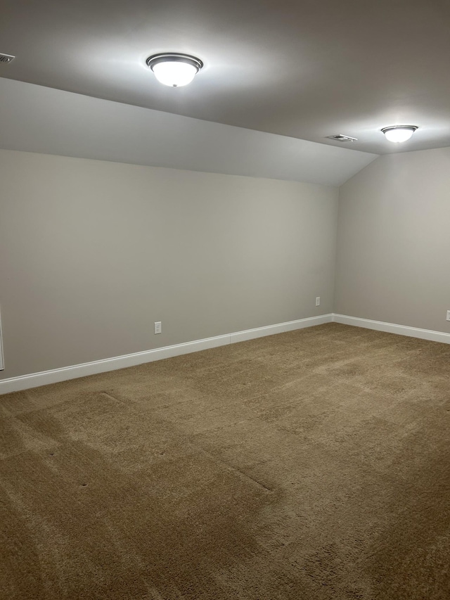 carpeted spare room featuring lofted ceiling, visible vents, and baseboards