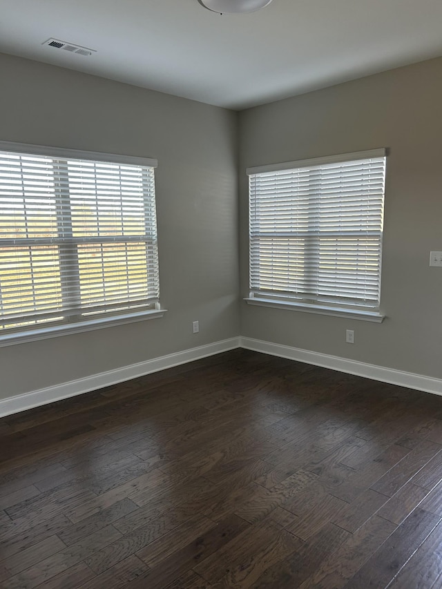 unfurnished room featuring dark wood-style floors, visible vents, and baseboards