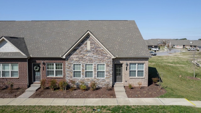 view of front facade featuring brick siding, stone siding, a front yard, and roof with shingles