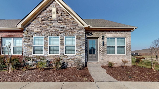 view of front facade with stone siding, brick siding, and a shingled roof