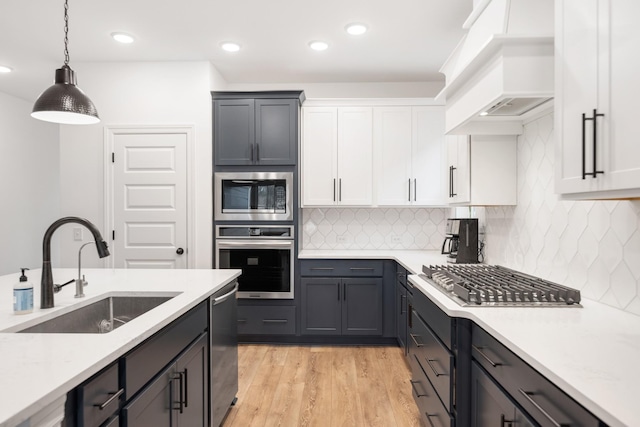 kitchen featuring sink, appliances with stainless steel finishes, custom range hood, pendant lighting, and white cabinets