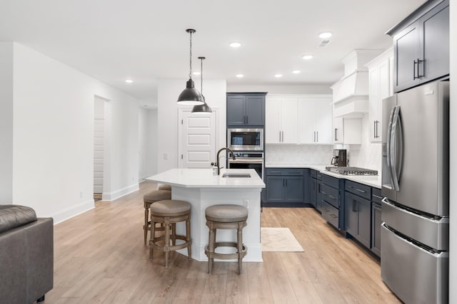 kitchen featuring sink, appliances with stainless steel finishes, hanging light fixtures, an island with sink, and white cabinets