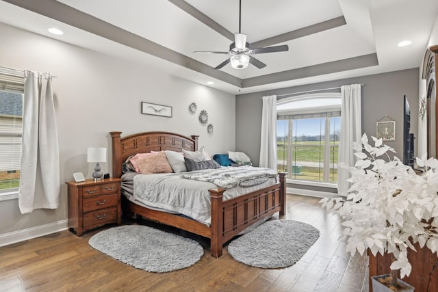 bedroom with hardwood / wood-style floors, ceiling fan, and a tray ceiling