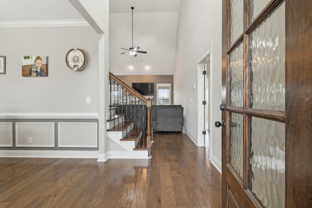 entryway with dark wood-type flooring, ornamental molding, ceiling fan, and a high ceiling