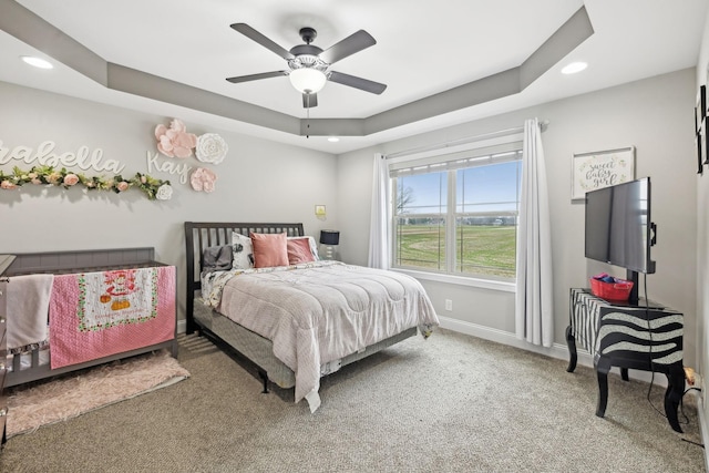 carpeted bedroom with a raised ceiling and ceiling fan