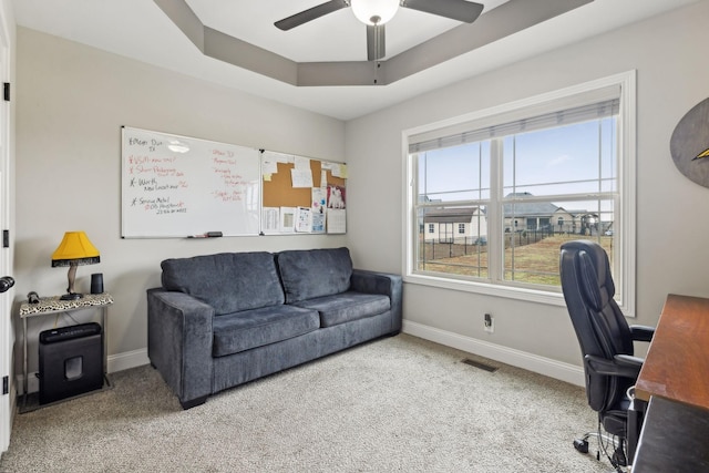 carpeted office space with a raised ceiling and ceiling fan