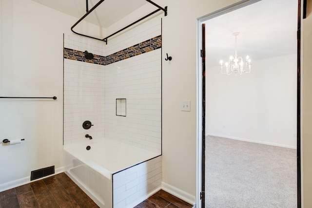 bathroom with hardwood / wood-style floors, tiled shower / bath combo, and a chandelier