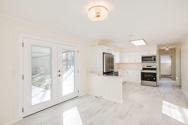 kitchen with stainless steel appliances, white cabinetry, light hardwood / wood-style floors, and french doors