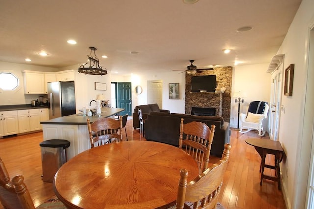 dining space with ceiling fan, a fireplace, sink, and light wood-type flooring