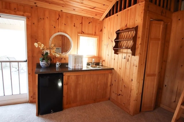 bar with vaulted ceiling, refrigerator, wood walls, sink, and light carpet