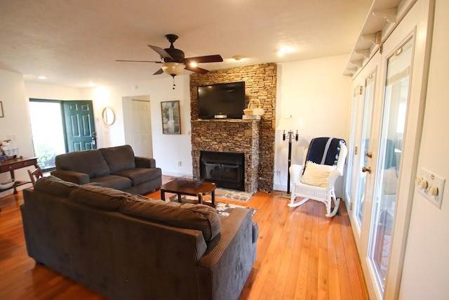 living room with hardwood / wood-style floors, a stone fireplace, and ceiling fan