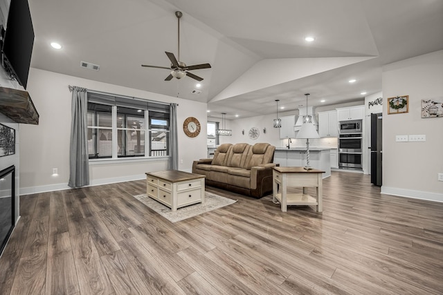 living room featuring ceiling fan, lofted ceiling, a large fireplace, and light wood-type flooring