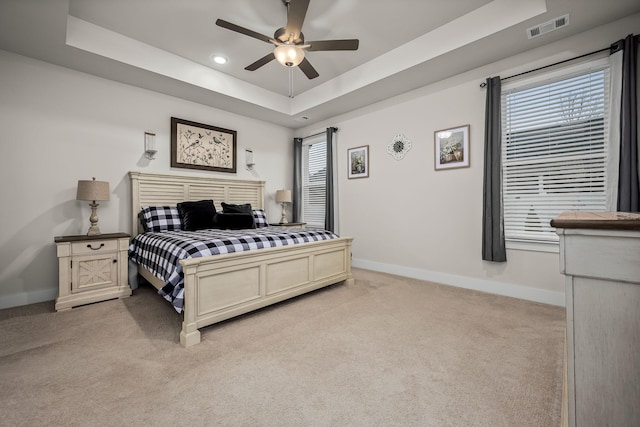 carpeted bedroom with ceiling fan, a tray ceiling, and multiple windows