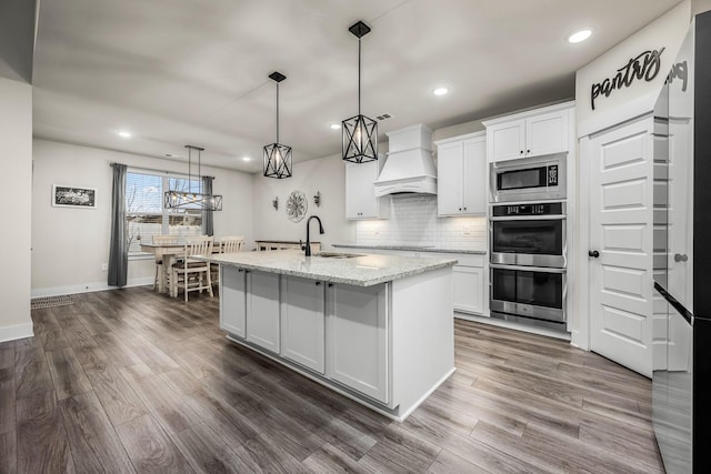 kitchen with sink, custom exhaust hood, white cabinetry, hanging light fixtures, and stainless steel appliances