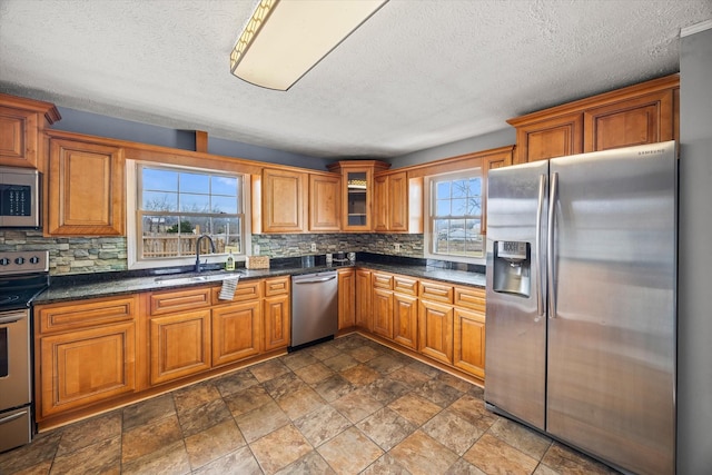 kitchen with stainless steel appliances, sink, decorative backsplash, and dark stone countertops