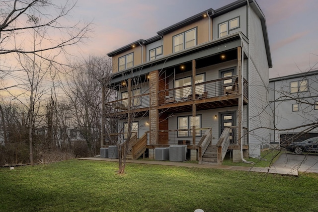 back house at dusk featuring a balcony, a yard, and central AC unit