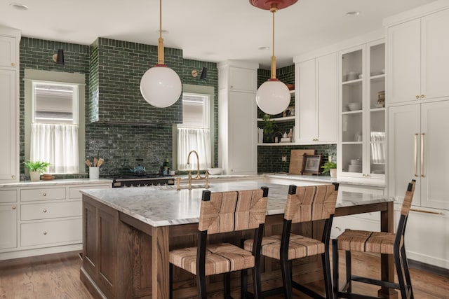 kitchen featuring backsplash, decorative light fixtures, and an island with sink