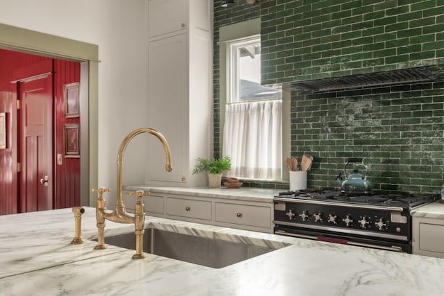 kitchen featuring white cabinets, sink, backsplash, and high end range oven