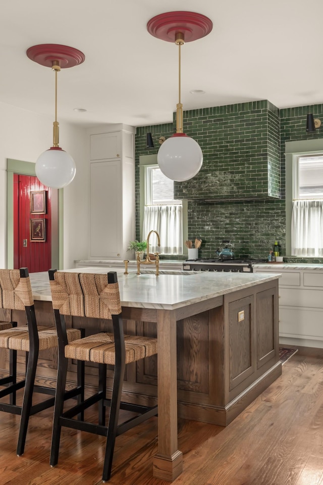 kitchen featuring sink, hanging light fixtures, hardwood / wood-style floors, decorative backsplash, and white cabinets