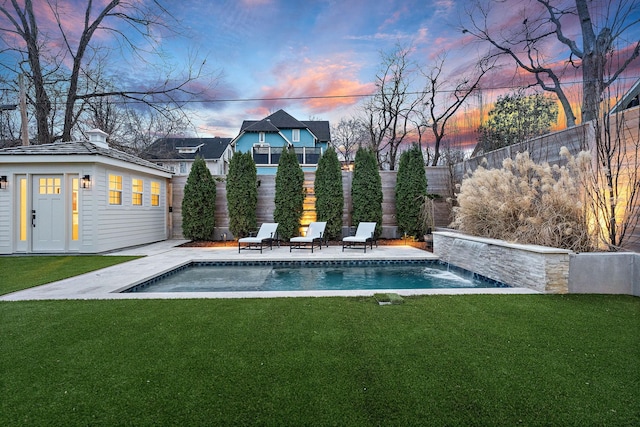 pool at dusk featuring pool water feature, a patio, an outbuilding, and a lawn