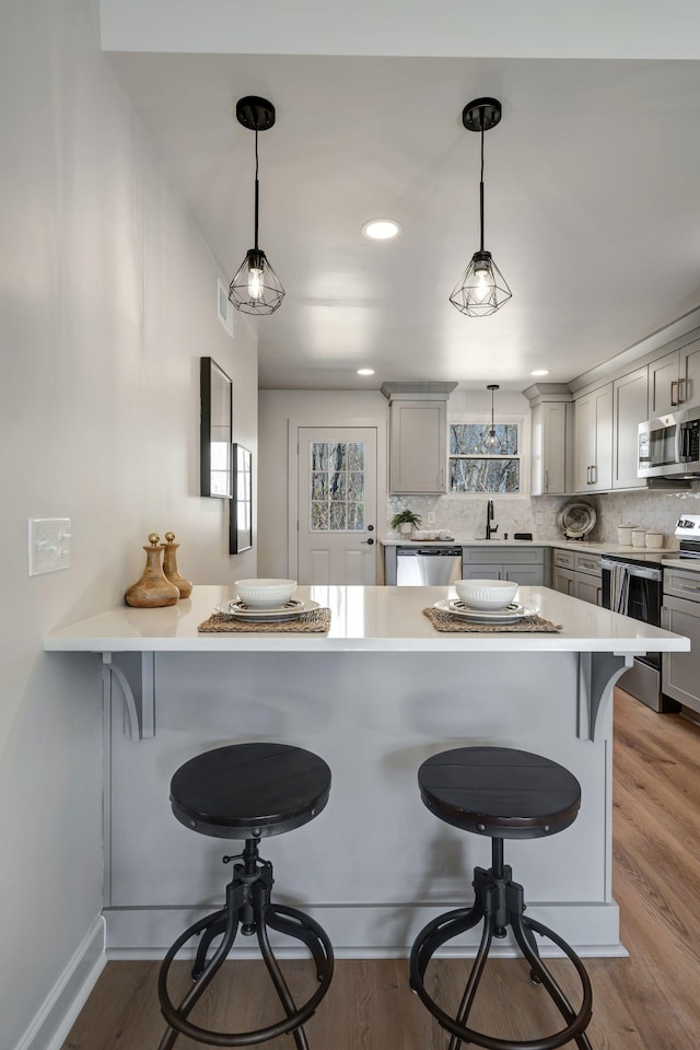 kitchen featuring a breakfast bar, gray cabinetry, hanging light fixtures, kitchen peninsula, and stainless steel appliances