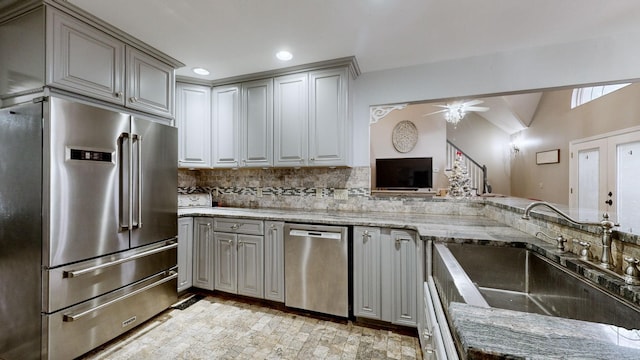 kitchen with sink, gray cabinetry, tasteful backsplash, light stone counters, and stainless steel appliances