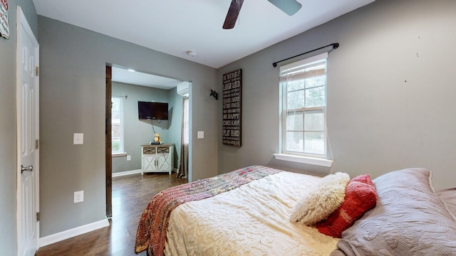 bedroom featuring ceiling fan, a wall mounted air conditioner, dark hardwood / wood-style floors, and multiple windows