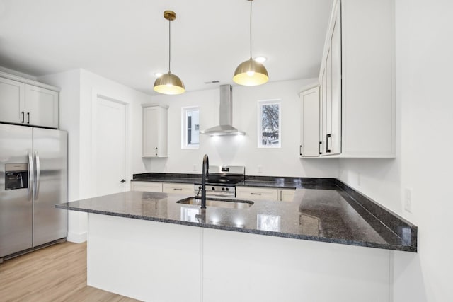 kitchen with sink, white cabinetry, decorative light fixtures, appliances with stainless steel finishes, and wall chimney range hood