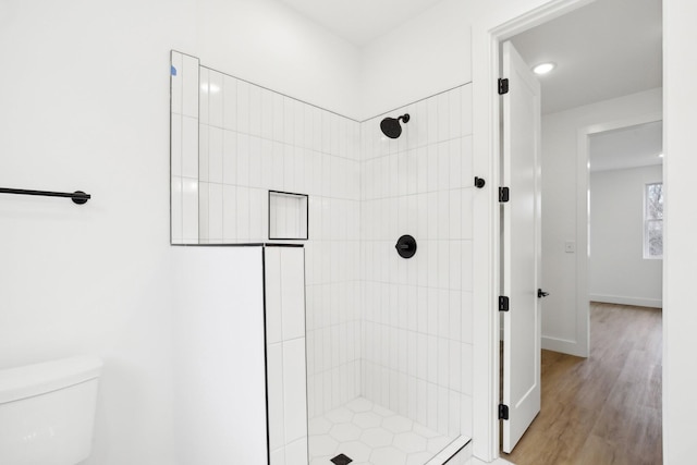 bathroom with hardwood / wood-style floors, toilet, and tiled shower