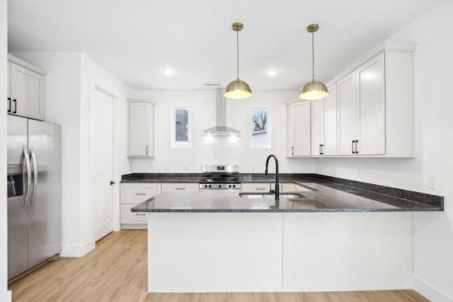 kitchen with wall chimney range hood, sink, stainless steel appliances, decorative light fixtures, and kitchen peninsula