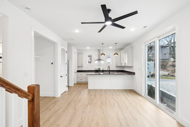 kitchen featuring pendant lighting, sink, white cabinets, wall chimney exhaust hood, and light hardwood / wood-style flooring