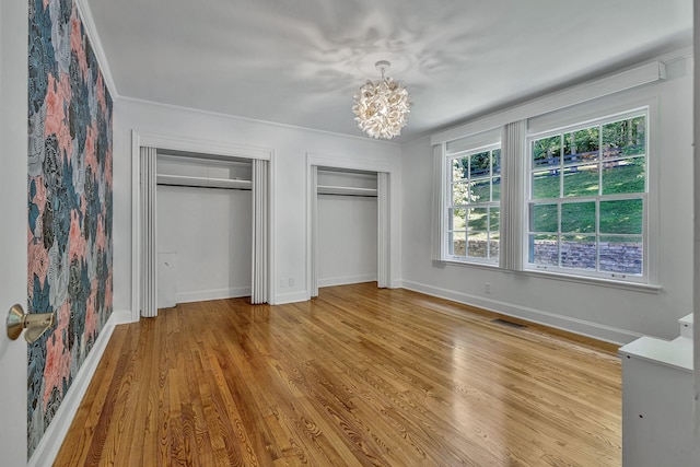 unfurnished bedroom with an inviting chandelier, ornamental molding, light hardwood / wood-style floors, and multiple closets