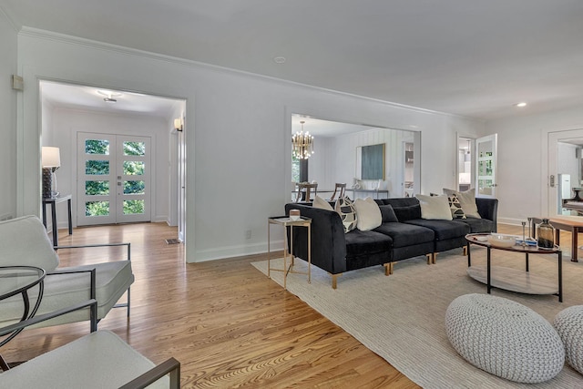 living room featuring french doors, ornamental molding, an inviting chandelier, and light wood-type flooring