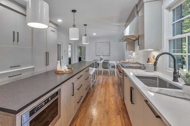 kitchen featuring sink, high end range, hanging light fixtures, range hood, and light hardwood / wood-style floors