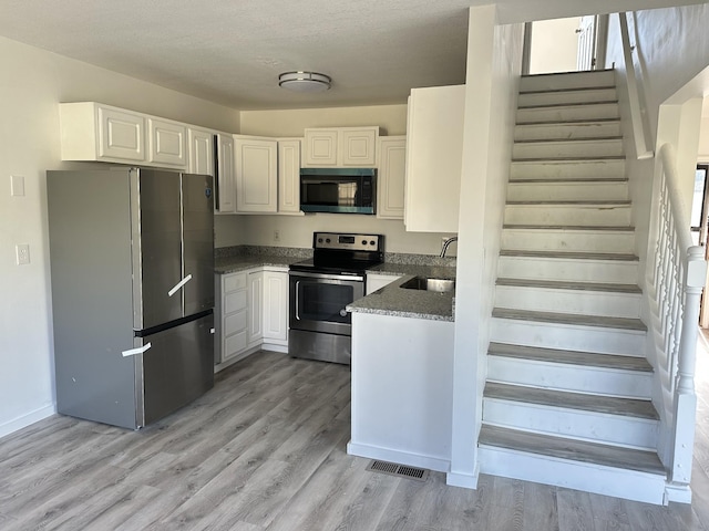 kitchen with visible vents, white cabinets, stainless steel appliances, light wood-style floors, and a sink