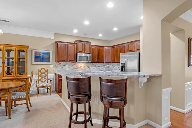 kitchen with sink, a breakfast bar area, backsplash, stainless steel appliances, and light stone counters