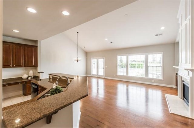 kitchen featuring vaulted ceiling, pendant lighting, sink, a kitchen bar, and dark stone counters