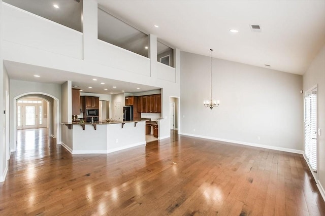 unfurnished living room featuring an inviting chandelier, wood-type flooring, and high vaulted ceiling