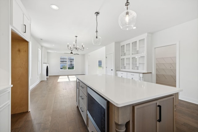 kitchen with hanging light fixtures, a center island, stainless steel microwave, white cabinets, and dark hardwood / wood-style flooring