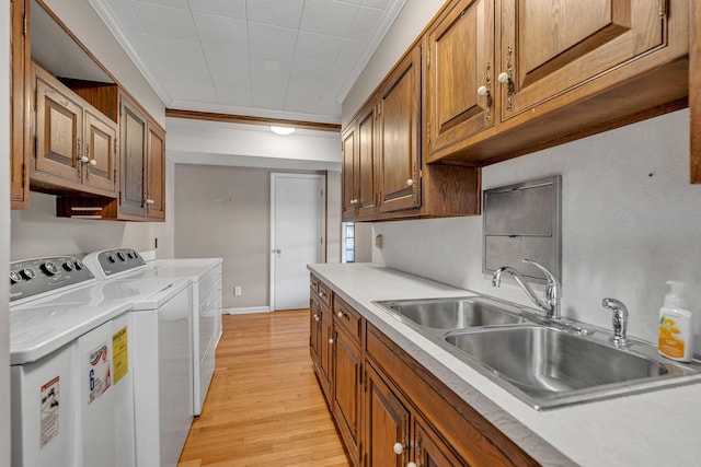 kitchen with independent washer and dryer, ornamental molding, sink, and light wood-type flooring