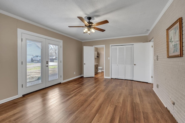 unfurnished bedroom with hardwood / wood-style flooring, access to outside, a textured ceiling, and brick wall