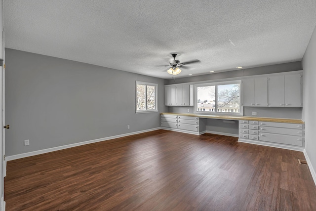 kitchen featuring dark hardwood / wood-style floors, built in desk, white cabinetry, ceiling fan, and a textured ceiling