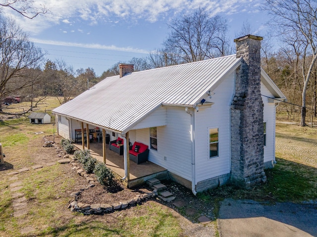 view of property exterior with metal roof, a patio, a chimney, and a standing seam roof