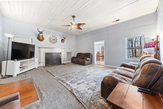 living room with visible vents, a ceiling fan, a fireplace with flush hearth, wood ceiling, and carpet flooring